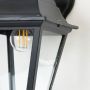 Closeup of outdoor wall lantern showing black metal body and clear glass panels highlighting fine details and texture.