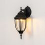 Black outdoor wall sconce with decorative finial illuminating porch creating traditional vintage coach style exterior lighting.