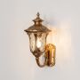 Antique gold outdoor wall lantern with clear textured glass glowing warmly on white background for classic exterior decor.