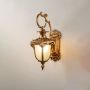 Antique outdoor wall light on white background highlighting golden finish and frosted glass shade.