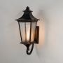 Large black carriage style outdoor wall lantern with ribbed glass panels with its light turned on against a plain light off-white background.