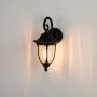 Illuminated classic black outdoor wall lantern casting a warm glow against a plain white studio background.