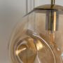 Closeup of amber glass globe pendant lamp highlighting glossy finish and metallic gold fitting for luxury lighting.
