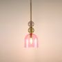 Modern glass pendant lights with pink and green shades hanging above a wooden table with a white vase and flower.
