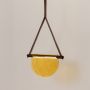 Pendant light with illuminated yellow half-moon glass shade and brown frame displayed on a clean white background for a bright look.