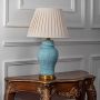 Blue ceramic lamp with pleated lampshade and golden base turned off on white background.
