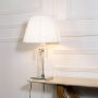Glass lamp with lights on featuring crystal accents chrome base and pleated white shade on plain white background.