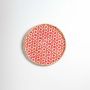 Round woven bamboo basket with red circular floral pattern on white background showcasing handmade decorative wall art.
