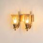 Illuminated pair of brass wall lamps with glowing amber textured glass shades and curved arms on white background.