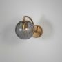 Brass wall light with smoky grey glass globe shade displayed against clean white wall backdrop.
