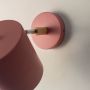 Closeup of pink wall lamp with smooth matte finish and wooden arm detail showing elegant and minimal craftsmanship.