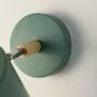 Detailed shot of the green metal cylindrical shade and the natural wood connecting arm of the modern wall sconce showing the texture and finish.