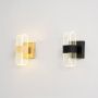 Gold wall lights with ribbed clear glass shades illuminated on a clean white background showing bright warm glow.
