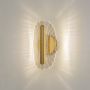 Gold wall light with clear acrylic patterned shade illuminated on a clean white background showing warm glow.