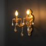 Golden 2 light wall light with crystal accents illuminated against black background for luxury home decoration.