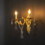 Golden wall light with dual candle style and crystal drops displayed on light black background for interiors.