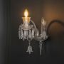 Crystal wall light with ornate glass design and crystal drops glowing warmly on black background view.