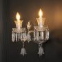 Double arm crystal wall light with detailed glass shades and crystal drops glowing on black background.