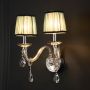 Double arm wall light with chrome base blue fabric shades and crystal accents glowing on black background.