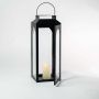 Tall black lantern lit displayed plain on white background highlighting glass and metal frame.