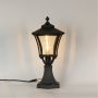 Black pillar lantern on white background with light on showing glowing textured glass and classic metal frame suitable for pathways patios and exterior decor.