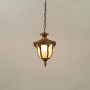 Illuminated antique gold outdoor pendant lantern with frosted glass panels glowing warm against a clean plain white studio background.