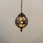 Illuminated black metal sphere pendant light with decorative cage design and warm bulb glowing against a plain white background.