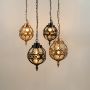 Group of four vintage style round cage pendant lights in black and gold finishes hanging together with warm lights on.