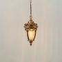 Antique gold metal hanging lantern with ribbed glass shade shown with lights on for classic indoor and outdoor decor.
