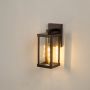 Bronze metal outdoor wall lantern light on with tall clear glass body and warm bulb glow ideal for porch patio balcony and entryway exterior lighting Decor.