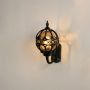 Black metal globe wall lantern with warm light on displayed against a white background showing its detailed frame and classic outdoor lighting style.