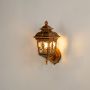 A gold outdoor wall lantern with lights on showcasing its warm glow and ornate design against a white background for a clear and elegant product display.