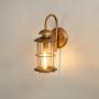 Gold outdoor lantern light displayed on a white background highlighting its curved arm and clear glass design.