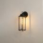 Black outdoor wall lantern shown on a white background featuring a tall glass frame and sleek metal structure.