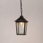 Illuminated black outdoor pendant lantern with warm LED bulb glowing through ribbed glass panels on clean white background.