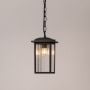 Black metal hanging lantern with ribbed glass glowing warmly on white background for outdoor porch and garden lighting.