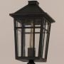 Close up view of black post light lantern head showing metal grid frame clear glass panels and warm vintage bulb.