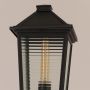Close up view of black post light lantern head showing ribbed glass panels metal frame and warm vintage bulb detail.