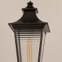 Closeup of black metal outdoor lamp post showing clear glass lantern and warm bulb detail for garden and pathway lighting.