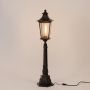 Black metal pillar lamp with warm glowing bulb and ribbed glass panels shown on white background for outdoor lighting.