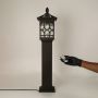 A decorative outdoor pillar lamp shown against a white background with the light off highlighting the metal structure and glass detailing in a clear product view.