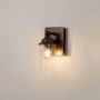 Bronze metal wall light glowing through a clear cylindrical glass shade ideal for indoor home decor.