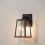 Black metal wall lantern with light on showing warm glow through clear glass ideal for outdoor walls and porch lighting.