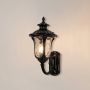 Black outdoor wall lantern glowing softly on white background showing bright light and textured glass for exterior decor.