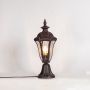 Antique brown pillar light with patterned clear glass glowing softly on white background for elegant outdoor lighting decor.